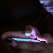 Close-up of a person using a glowing smartphone in a dark room