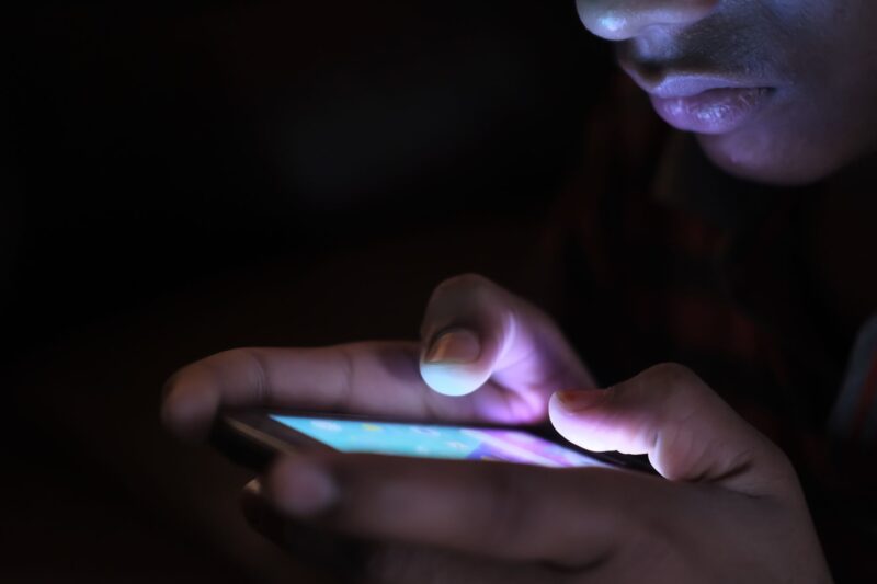 Close-up of a person using a glowing smartphone in a dark room