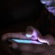 Close-up of a person using a glowing smartphone in a dark room
